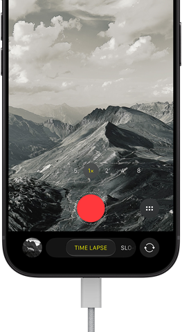 iPhone 18 Pro, front exterior, displaying a mountainous landscape, with the camera mode overlay in Time-Lapse mode, with power cable attached to charging port